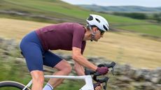 Man wearing a purple jersey, blue cycling shorts and a white helmet riding a white bike downhill